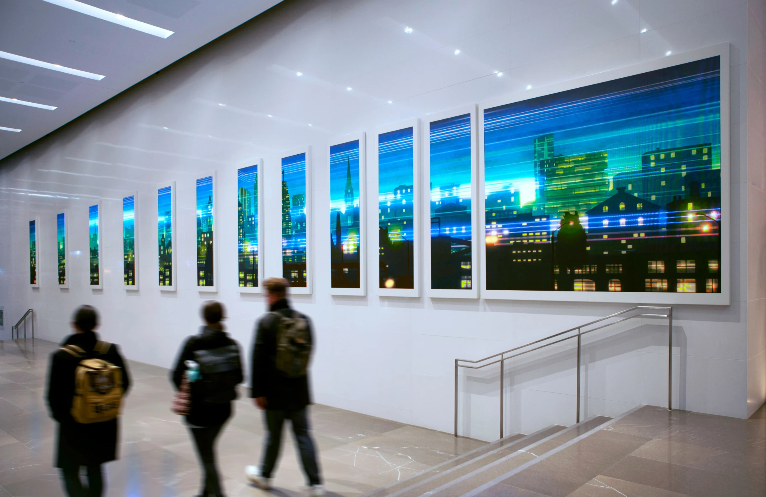 People walk past a series of vertical artworks depicting a colourful abstract cityscape at night.